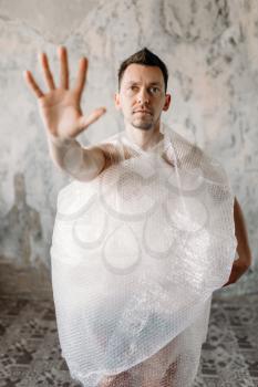 Freak man wrapped in packaging bubble film pulls his hand. Funny guy in abandoned house