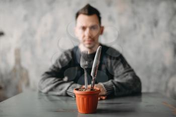 Autistic man sitting against pot with fork and knife instead of plants. Alone guy in abandoned house, autism syndrome