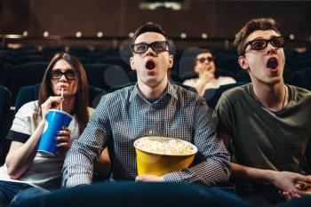 Surprised people in 3d glasses with popcorn and drinks watching movie in cinema. Entertainment business