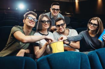 Happy friends with popcorn and drinks watching movie in cinema. Entertainment business