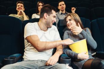 Smiling couple eats popcorn while watching movie in cinema. Showtime, comedy film