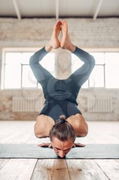 Male yoga standing on hands upside down. Exercise on mat in gym with grunge interior. Fit workout indoors