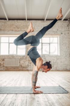 Male yoga standing on hands upside down. Exercise on mat in gym with grunge interior. Fit workout indoors
