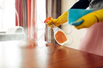 Housemaid hands in gloves cleans the table with a cleaning spray, hotel room interior on background. Professional housekeeping, charwoman
