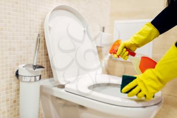Maid hands in rubber gloves cleans the bidet with a cleaning spray, hotel restroom interior on background. Professional housekeeping service, charwoman, sanitary processing