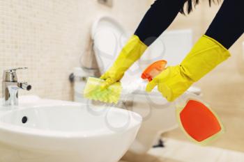 Maid hands in rubber gloves cleans the bidet with a cleaning spray, hotel restroom interior on background. Professional housekeeping service, charwoman, sanitary processing
