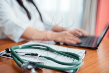 Stethoscope on wooden table closeup, family doctor concept, specialist works on laptop on background. Professional healthcare