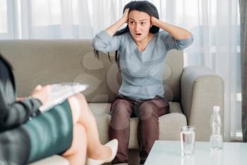 Female patient sitting on sofa at psychotherapist reception. Female doctor writes notes in notepad, professional psychology support