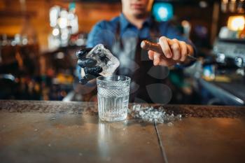 Male bartender pours a drink into a glass with ice. Barman at the bar counter. Alcohol beverage preparation