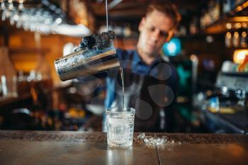 Male bartender in apron pours a drink into a glass. Barman at the bar counter. Alcohol beverage preparation