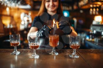 Female bartender making coctail with the use of fire. Alcohol drink preparation. Barman working at the bar counter in pub