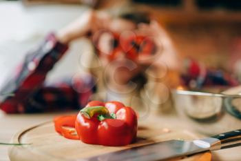Fresh red pepper closeup, housewife in an apron indulges on background. Female cook making healthy vegetarian food, salad cooking
