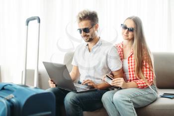 Couple looks on laptop screen, fees on journey concept. Luggage preparation. Travelling or tourism