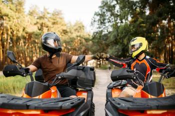 Two atv riders in helmets hits fists for good luck before dangerous extreme offroad riding, front view, summer forest on background. Freeriding on quad bike, quadbike adventure