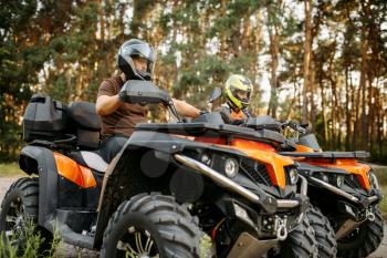 Two quad bike riders in helmets and equipment, side view, closeup, summer forest on background. Male quadbike drivers, atv riding, extreme sport
