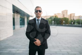 Male bodyguard in suit, security earpiece and sunglasses outdoors. Professional guarding is a risky profession