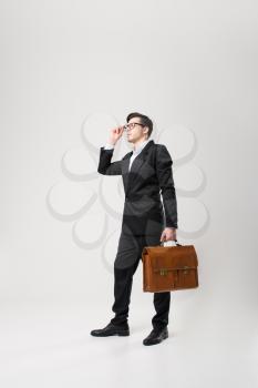 Businessman in glasses and black suit holds brown leather briefcase in hand isolated on white background