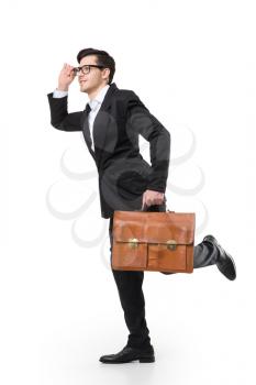 Young business man in glasses and black suit holds brown leather briefcase in hand and look into the distance, isolated on white background