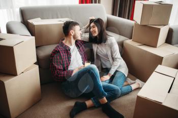Happy couple sitting between cardboard boxes, moving to new house. Relocation to apartment