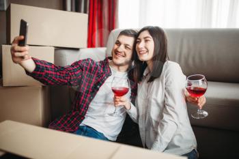 Young couple makes selfie against cardboard boxes, moving to new house. Relocation to apartment celebration