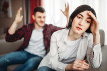 Stressed wife sits on couch, angered husband yells on her, family conflict. Unhappy man and woman in quarrel