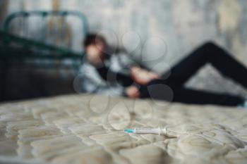 Syringe on the bed, junkie sleeping after dose on background. Drug addiction concept, narcotic addicted people