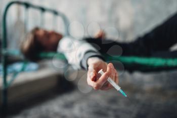 Male druggy with syringe in hand sleeping in bed after dose. Drug addiction concept, narcotic addicted people