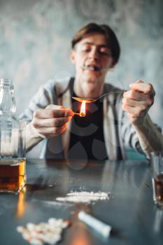 Drug addict with a spoon and matches prepares a dose. Narcotic addiction concept, addicted people, junkie