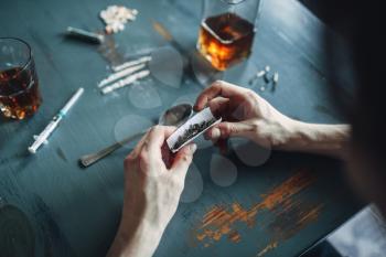 Drug addict hands prepares a dose, top view, bottle of alcohol and syringe on the table on background. Narcotic addiction concept, addicted people, junkie