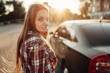 Young cheerful woman driver posing against a car. Female person and vehicle, automobile driving concept