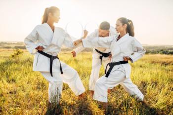 Two female karate fighters in white uniform with black belts on training fight in summer field. Martial art workout outdoor, technique practice