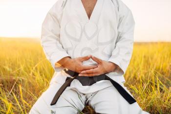 Male karate fighter sitting on the ground in summer field. Martial art training outdoor