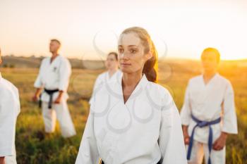 Martial art school on workout outdoor, technique practice. Group of fighters in uniform on training in the field on sunset