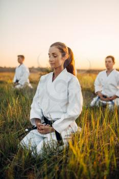 Karate class in white kimono meditates on training in summer field. Martial art workout outdoor, technique practice