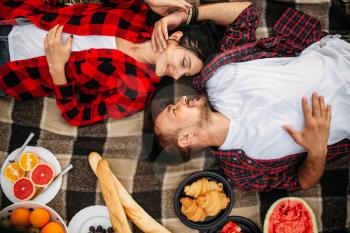 Love couple lies on plaid, top view, picnic in summer field. Romantic junket of man and woman