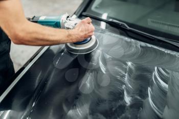 Male person with polishing machine cleans car hood. Auto detailing on carwash service, restore the paint of vehicle
