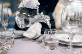 Waitress in gloves pours drinks into glasses, table setting. Serving service, festive dinner decoration, holiday dinnerware