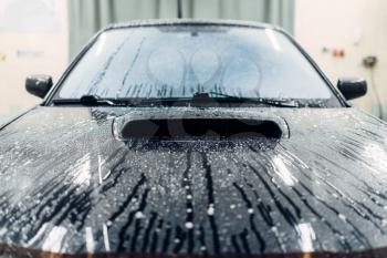 Carwash service, car covered with foam, front view. Auto detailing, high pressure washing on special station