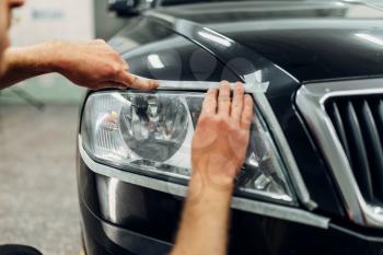 Auto detailing of car headlights on carwash service. Worker prepares glass for polishing