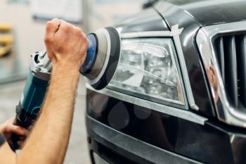 Auto detailing of car headlights on carwash service. Man works with polishing machine