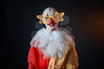 Mad bloody clown with makeup in carnival costume and holiday glasses, crazy maniac, scary monster