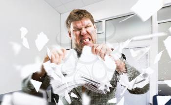 Angry businessman tearing stacks of paper in office. Mad businessperson works with documents, bad emotion, stress