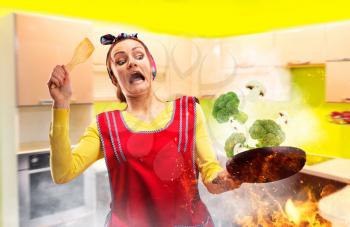 Crazy housewife in apron cooking broccoli on fire, kitchen interior on background. Funny female person with a frying pan, work is not going according to plan