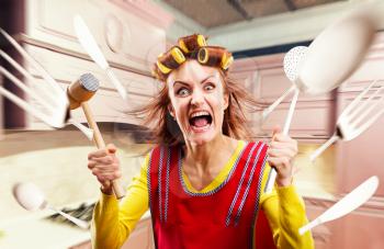 Crazy housewife in apron cooking, cookware flying around, kitchen interior on background. Mad female person with crockery