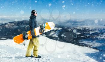 Male snowboarder with board stands on top of a snowy mountain. Snowboarding is an extreme winter sport. Man with snowboard before the dangerous downhill