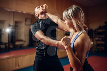 Female person on self-defense workout with male personal trainer, gym interior on background. Woman makes punch to the throat on training, self defense practice