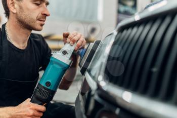Auto detailing of car headlight on car-wash service. Man works with polishing machine