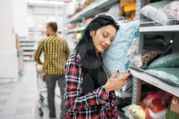 Young couple choosing pillow in supermarket. Male and female customers on family shopping. Man and woman purchasing goods for the house