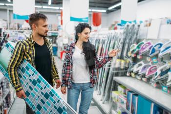 Young couple choosing electric iron in supermarket. Male and female customers on family shopping. Man and woman purchasing goods for the house