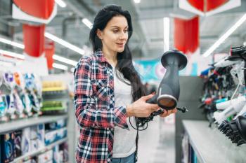 Young woman choosing hairdryer in supermarket. Female customer on shopping in hypermarket